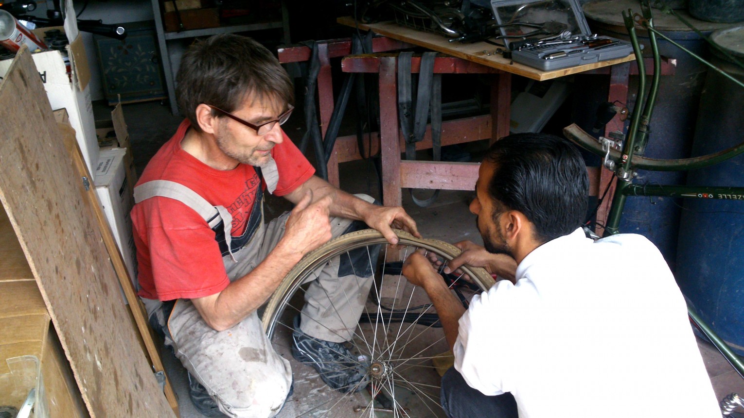 Mann in Handwerkerkleidung und Mann aus Syrien beim Fahrradreifen reparieren.
