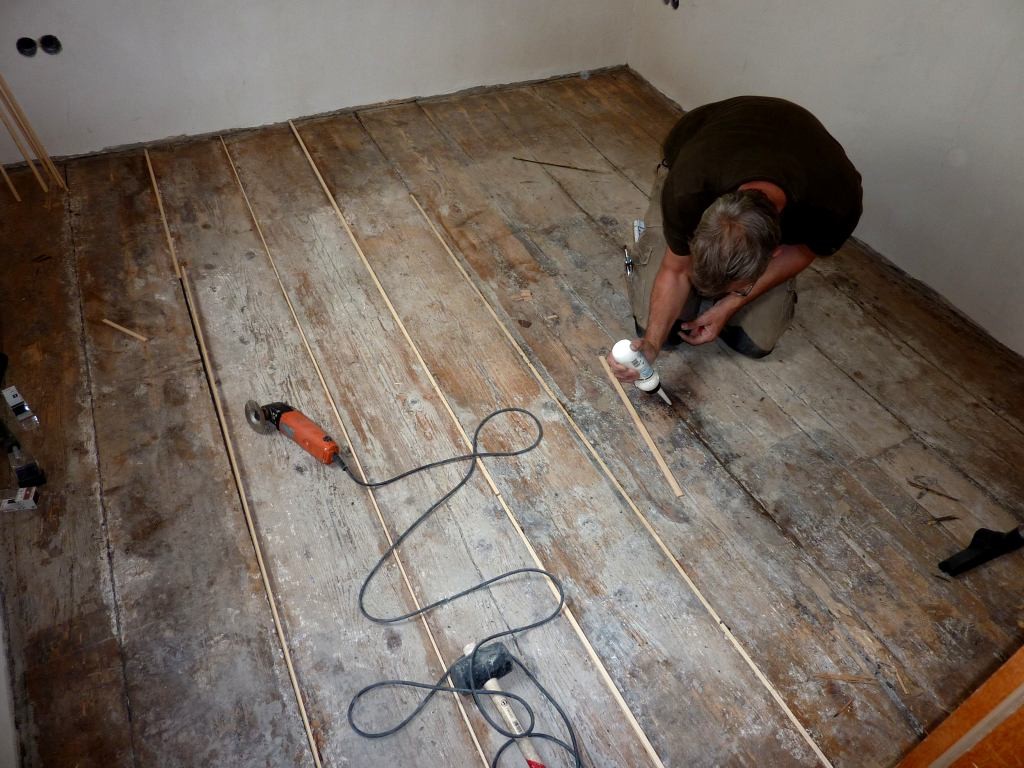 Handwerker fügt neue Weichholzleisten in alten Dielenboden ein.